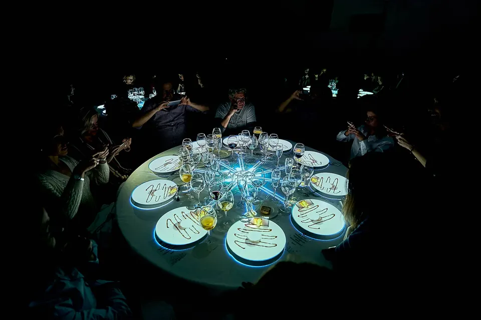 Cena de gala de empresa en un gran salón con mesas redondas iluminadas y escenario