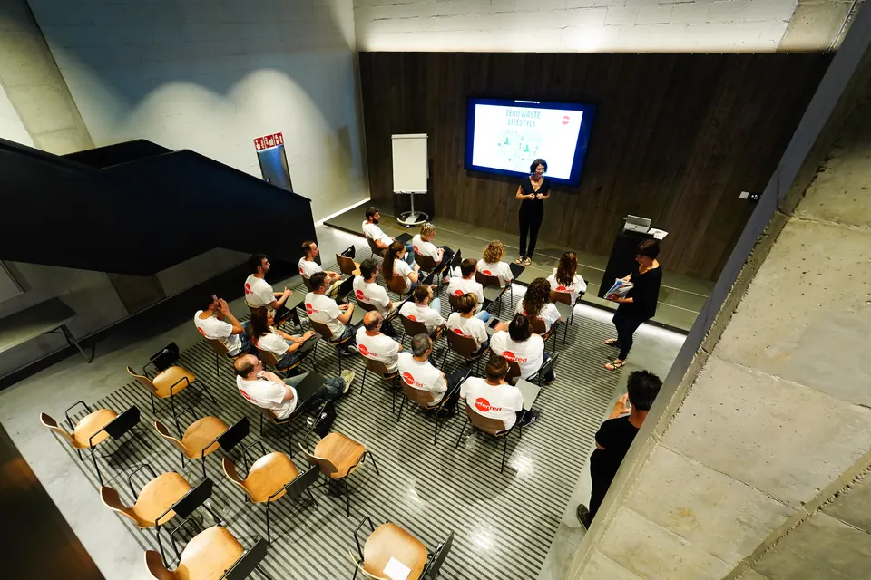 Seminario de formación con asistentes en mesas de trabajo, pizarra blanca y una facilitadora de pie
