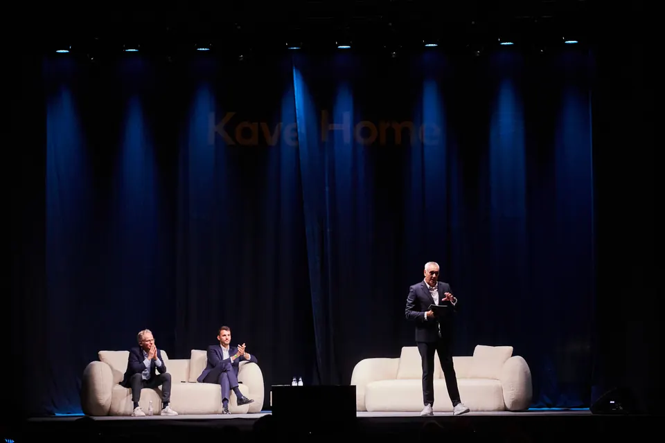 Escenario de una convención experiencial con iluminación cálida y asistentes sentados en un espacio industrial rehabilitado
